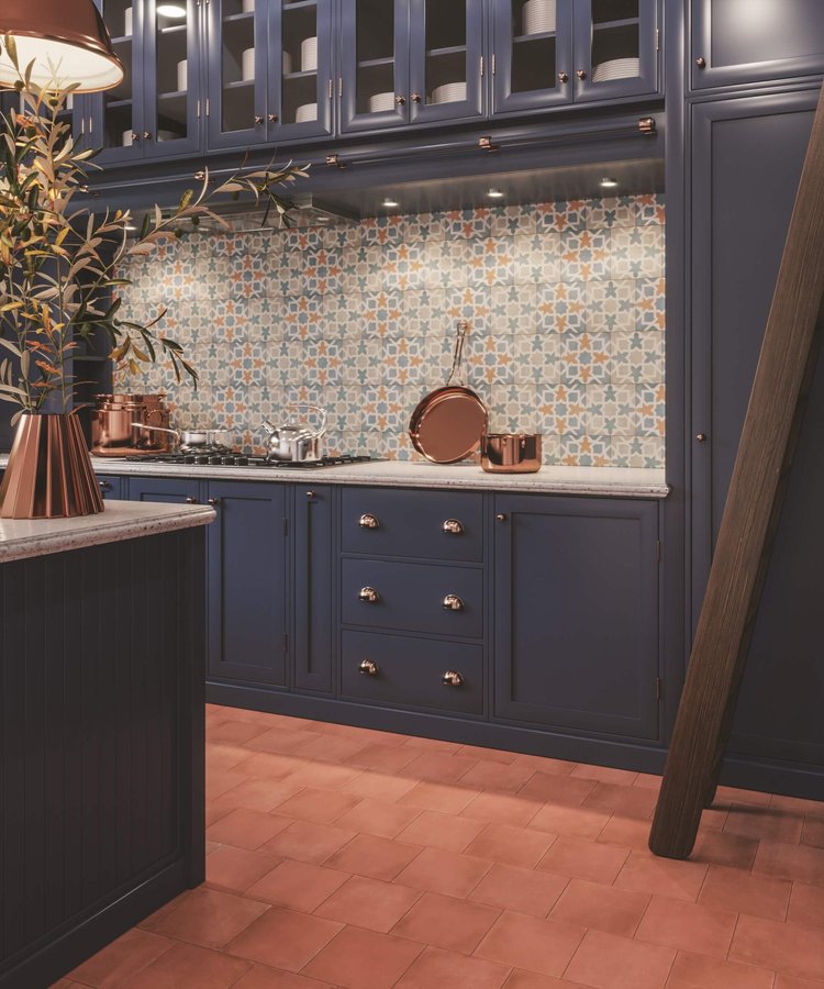 The strong deco pattern of the backsplash tile beautifully coordinates with the blue cabinetry and the terra cotta of the square floor tile.